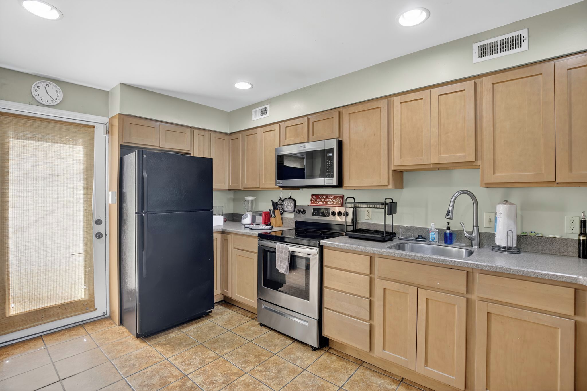 A modern kitchen with wooden cabinets, a stainless steel refrigerator, a microwave, a stove, and a sink.