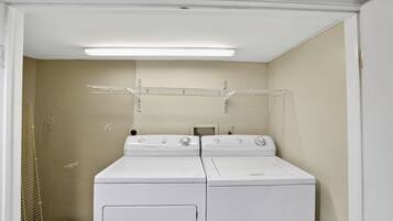 A laundry room with two stacked washers and dryers, a metal drying rack, and a small heater.
