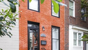 A red brick building with a black door, a small porch, and two green trash bins. - Hudson house (Baltimore)