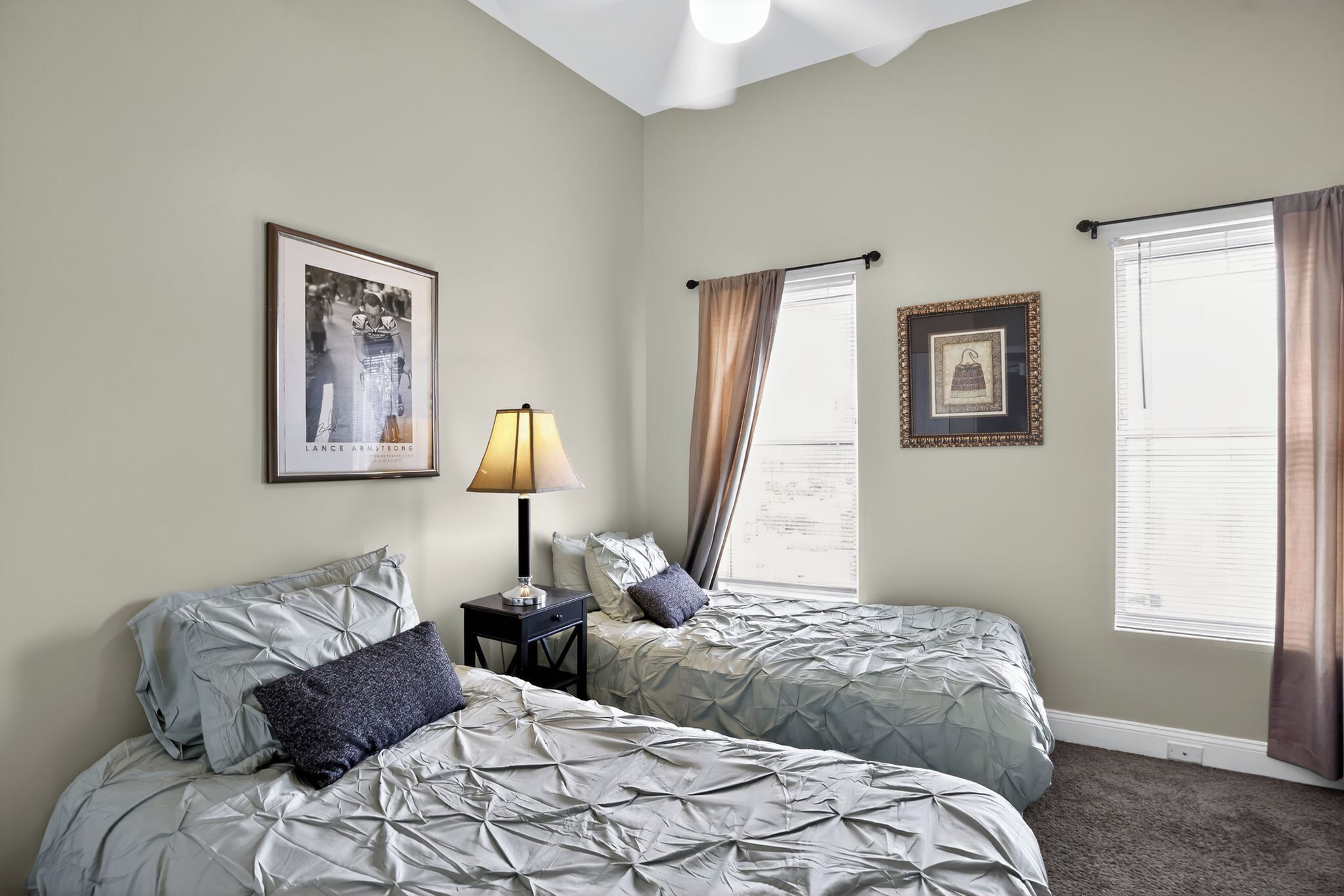 A bedroom with two beds, a nightstand, a lamp, and framed pictures on the walls.