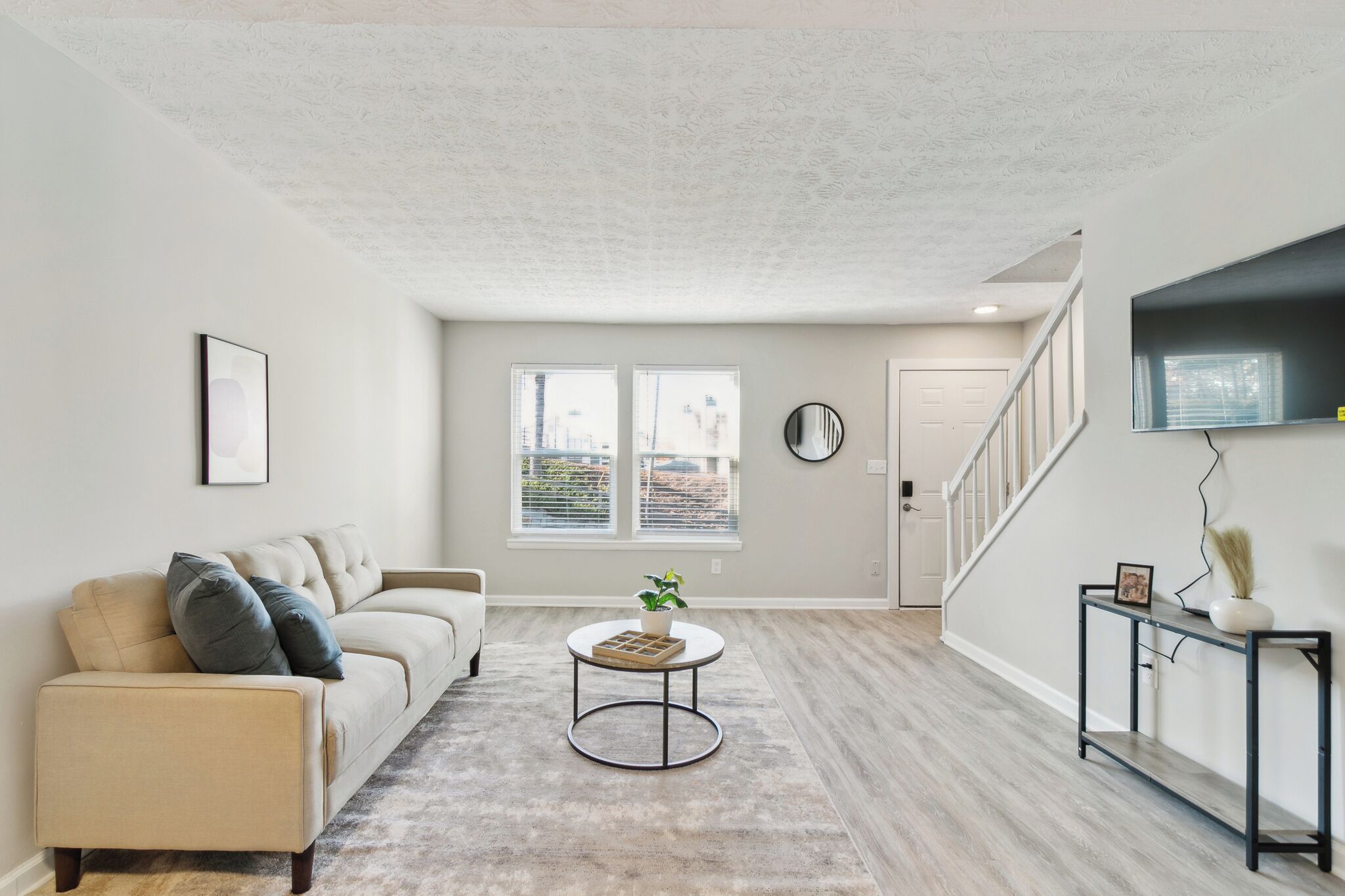 A living room with a beige sofa, a round coffee table, and a staircase leading to another level.