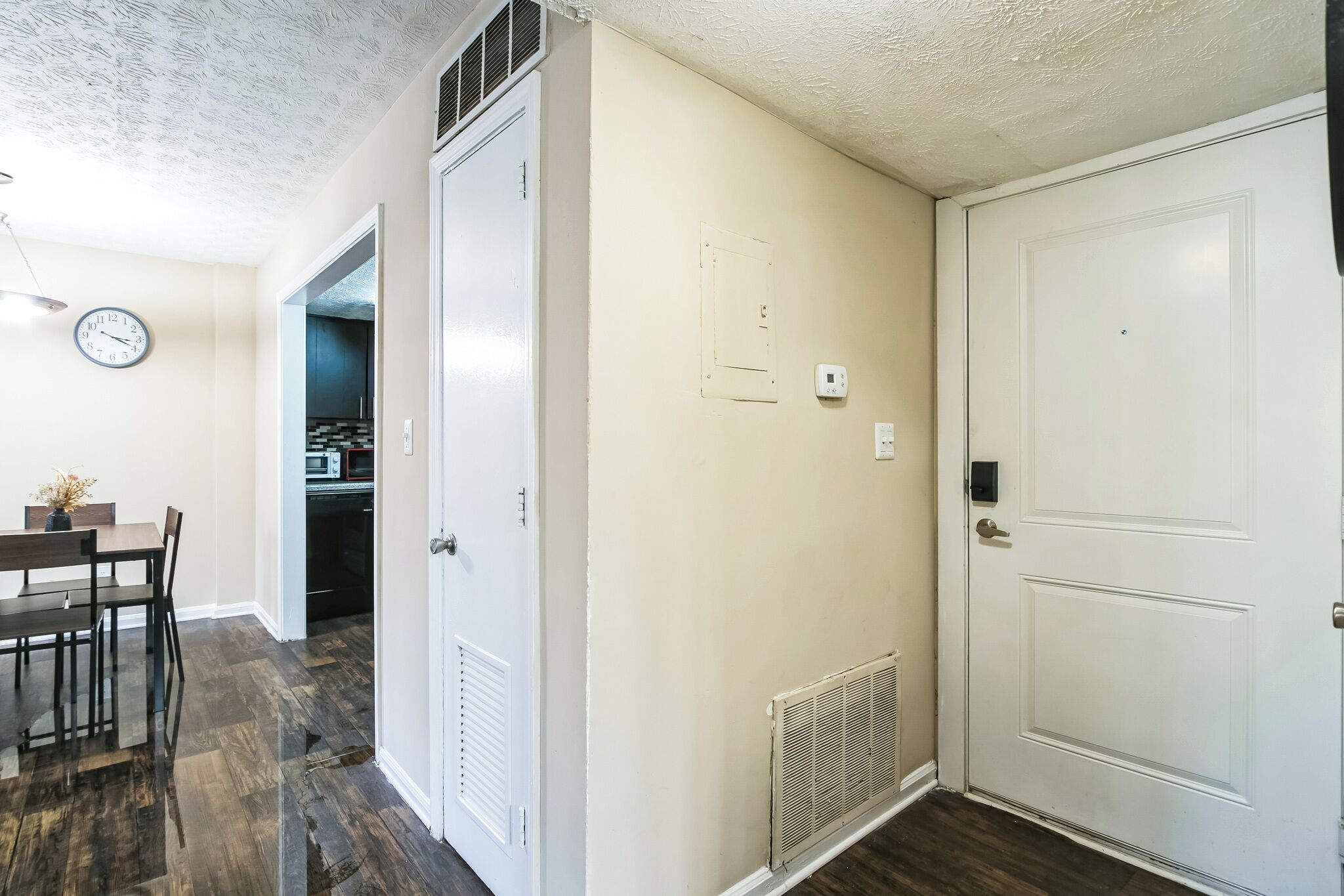 A hallway with a dining area, a clock, and a microwave.