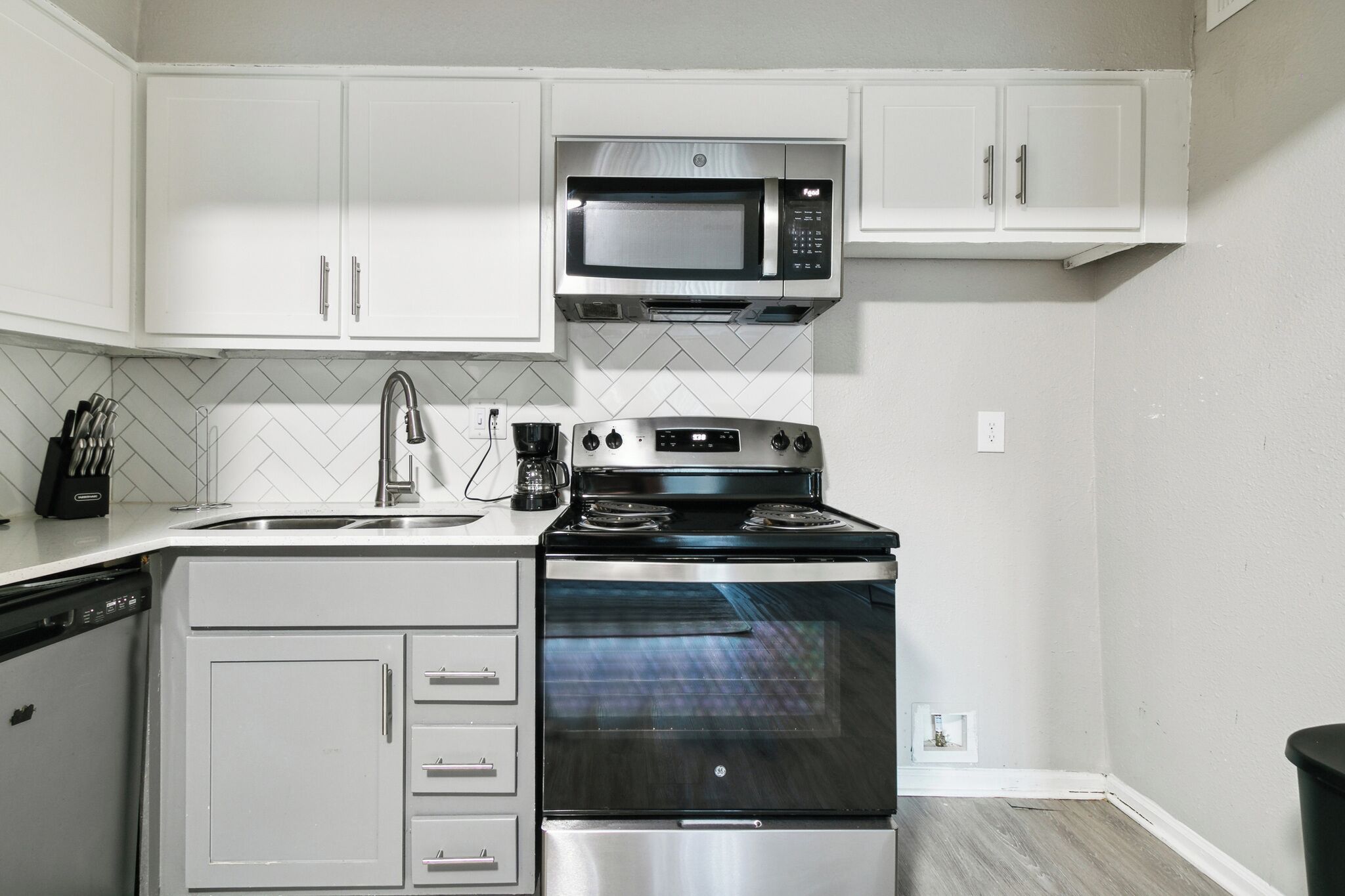 Una cocina compacta con gabinetes blancos, un microondas de acero inoxidable, una estufa y un lavavajillas.