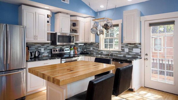 A modern kitchen with white cabinets, a wooden island, stainless steel appliances, and a view through a glass door. - Back Alley Apartment, walk Downtown and Duke. (Durham)