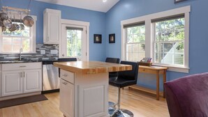 A modern kitchen with white cabinets, a wooden island, and a dining area with a table and chairs. - Back Alley Apartment, walk Downtown and Duke. (Durham)