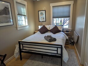 Un lit bien fait, avec des oreillers et des serviettes enroulées, une table de chevet avec une lampe et des œuvres d’art encadrées accrochées au mur.