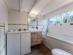 A modern bathroom with a bathtub, a sink, and a toilet. There is a window providing natural light and a view of the outside.