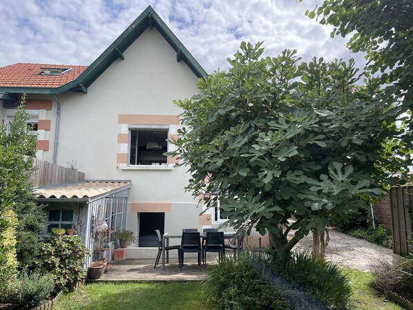 A house with a sloped roof, a small front porch, and a garden with various plants and a tree.