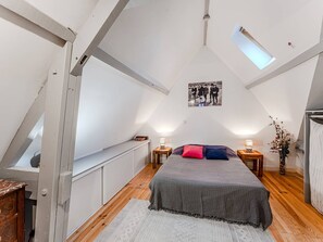 A bedroom with a sloped ceiling, a skylight, a bed with pillows, a nightstand, a vase with flowers, and a framed picture on the wall.