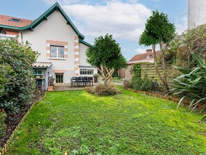 A house with a garden, a patio with chairs, and a small shed.