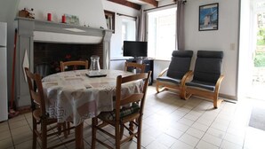 Ein gemütliches Wohnzimmer mit Kamin, Esstisch mit Stühlen, Fernseher und zwei Sesseln.