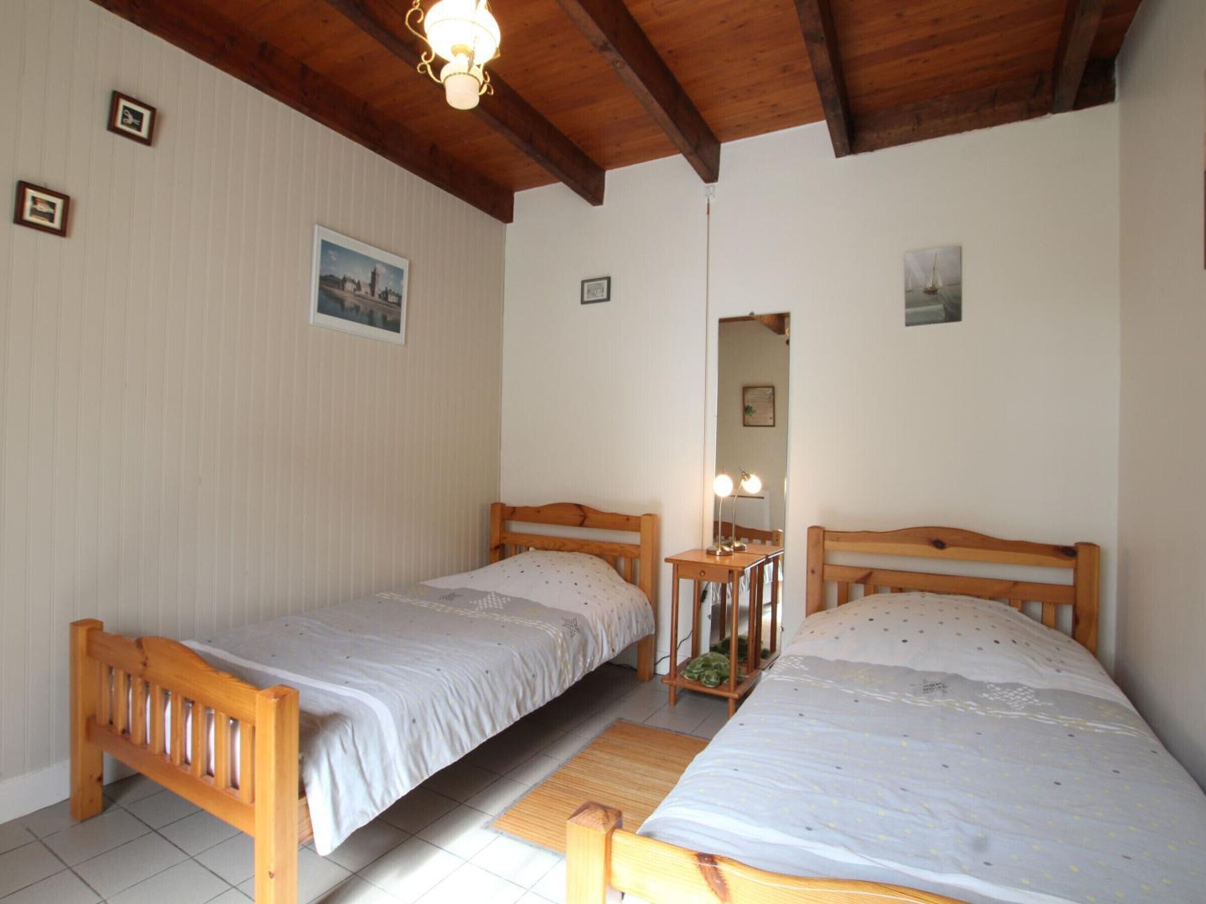 Ein Zimmer mit zwei Holzbetten, einem kleinen Tisch mit Spiegel und einer Deckenleuchte.