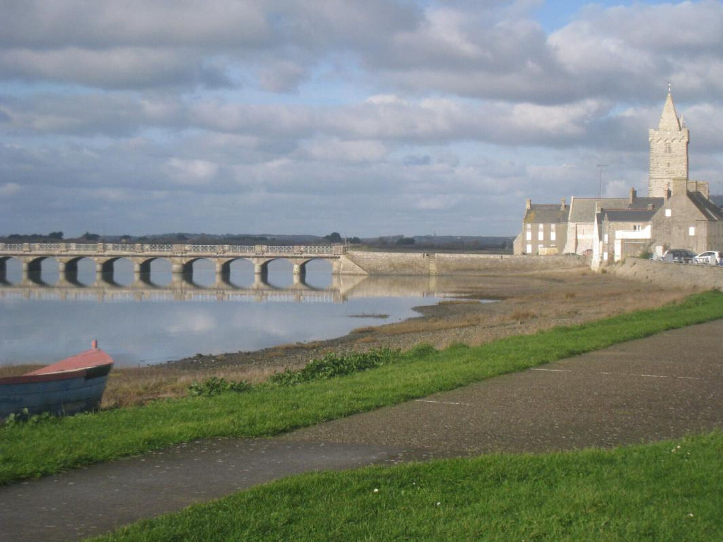 Uitzicht op een rivier met een stenen brug, een kerk en een rij huizen.
