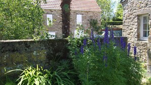 Ein Gebäude aus Stein mit roten Ziegeldach, umgeben von üppigem Grün und violetten Blumen.