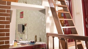 Eine Holztreppe führt zu einer erhöhten Ebene, einem Essbereich mit Backsteinwand und einem Kronleuchter.