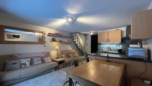 A compact living space with a sofa, a dining table, a kitchen area, and a staircase.
