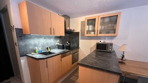 A compact kitchen with wooden cabinets, a black countertop, a microwave, a toaster, and a small table with a lamp.