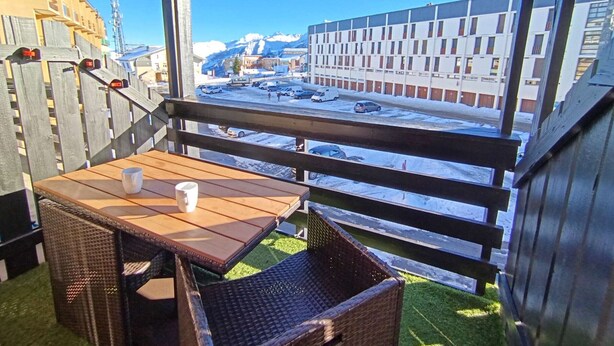 Een balkon met een tafel en stoelen, uitkijkend op een parkeerplaats en gebouwen, met een berg op de achtergrond.