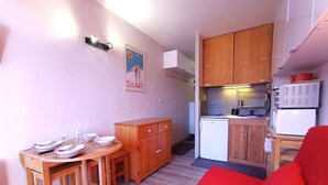 Een knus woongedeelte met een eethoek, kitchenette en een rode bank.