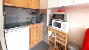 Een compacte keuken met houten kastjes, een ingebouwde oven, een magnetron en een klein wijnrek.