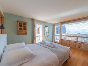 A bedroom with a large bed, a wooden cabinet, a mirror, and a window with blinds.