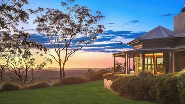 Una casa moderna con un porche cubierto, rodeada de césped cuidado y árboles, con vistas al horizonte.