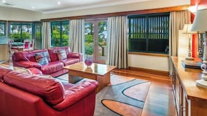 Un salón espacioso con un sofá de cuero rojo, una mesa de centro de madera y una zona de comedor con mesa y sillas.
