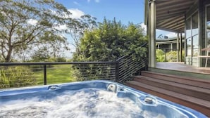 Un jacuzzi en una terraza de madera con vistas a árboles y un edificio con grandes ventanales.