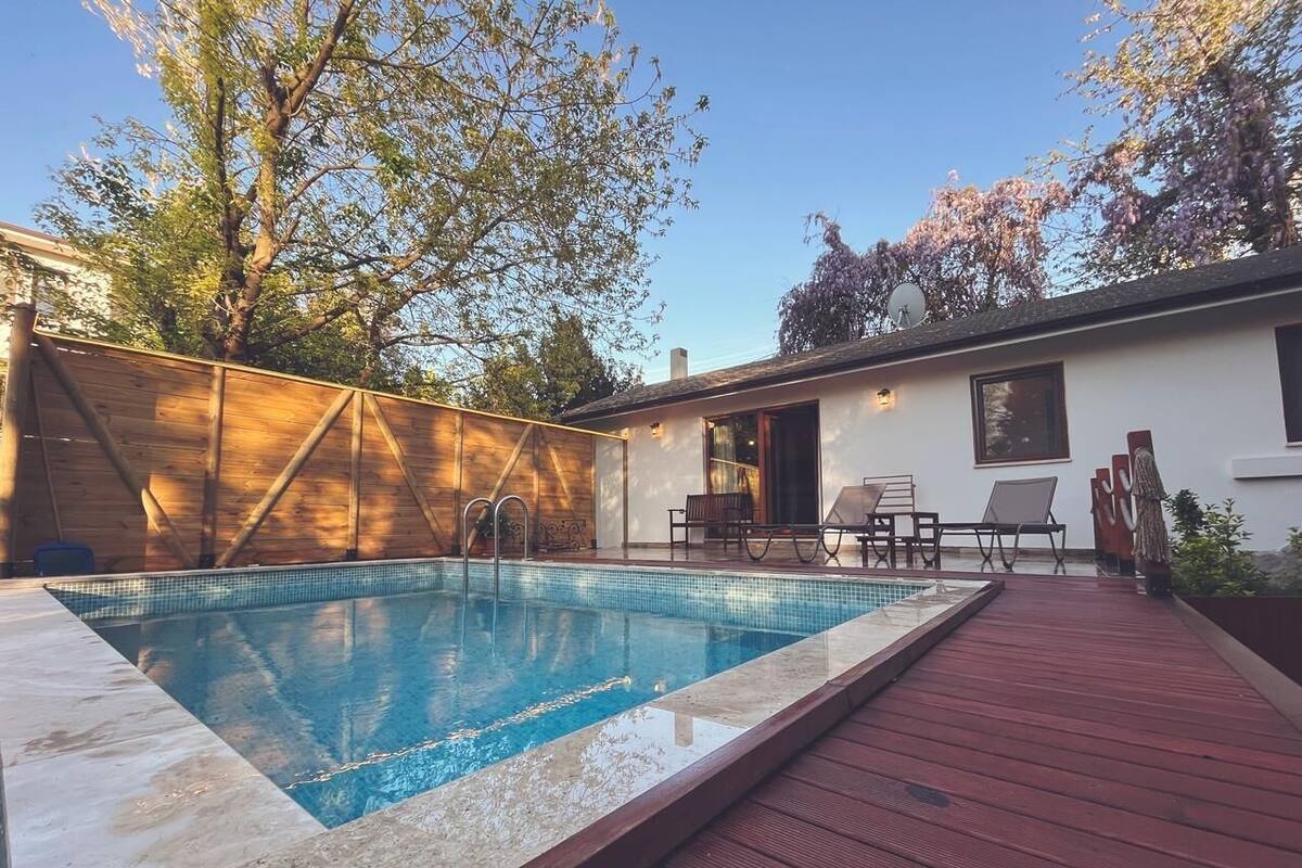 Une piscine avec une terrasse en bois, un patio couvert et un espace détente avec des chaises et une table.