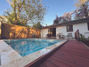 Une piscine avec une terrasse en bois, un patio couvert et un espace détente avec des chaises et une table.