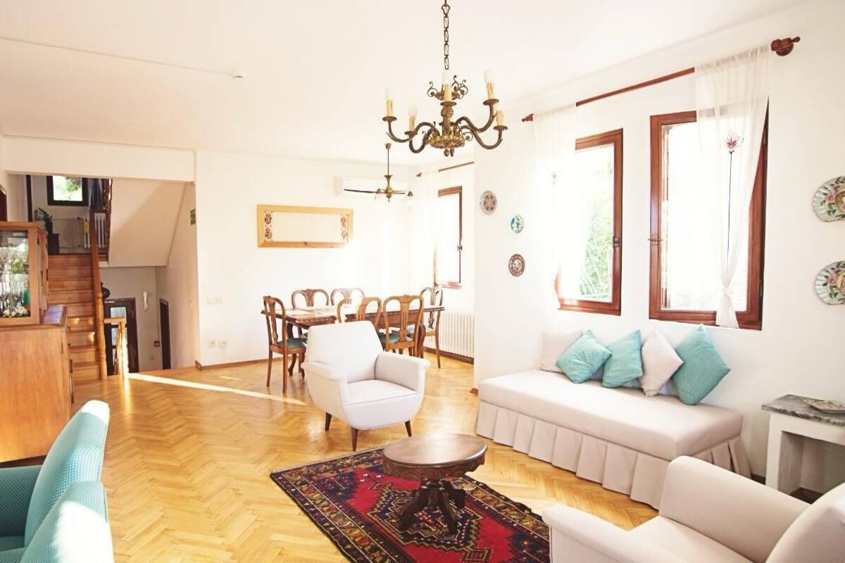 Un salon spacieux doté d’un parquet, de canapés blancs, d’un coin repas avec une table et des chaises en bois, et d’un lustre.