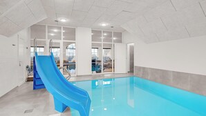 Sisätiloissa sijaitseva uima-allas, jossa on sininen liukumäki, suuret ikkunat ja korkea katto.
