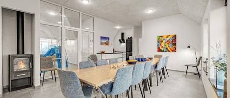 A modern dining area with a long table, blue chairs, a fireplace, and a staircase leading to an upper level.