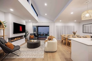 A modern living room with a flat-screen TV, a fireplace, and a dining area with a large table and chairs.