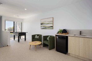 A modern kitchen with a foosball table, two green armchairs, a round wooden table, and a dishwasher.