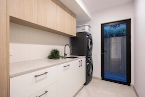 Una cuina moderna amb armaris blancs, una rentadora integrada i una petita planta al taulell.