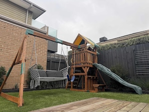 A wooden swing set, a rope swing, and a slide in a backyard.