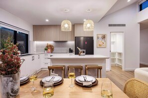 A modern kitchen with a central island, pendant lighting, and a dining area set for four.