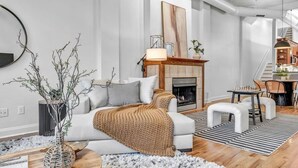 A modern living room with a fireplace, a white sofa, and a dining area with chairs.