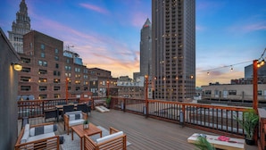 A rooftop deck with outdoor seating, a view of city buildings, and string lights.