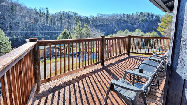 Une terrasse en bois avec une rambarde, deux chaises et une vue sur une zone boisée.