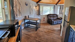 L’intérieur chaleureux d’un chalet avec un plafond en bois, une table à manger avec des bancs, un fauteuil inclinable et un réfrigérateur.