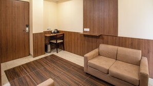 Una stanza con pavimento in legno, un divano beige, una scrivania con una sedia e un cestino.