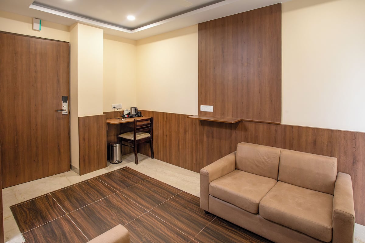A room with a wooden floor, a beige sofa, a desk with a chair, and a trash bin.