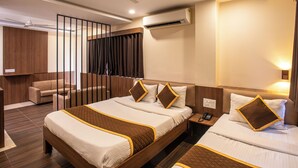 Camera d'albergo con un letto grande, un letto più piccolo, una scrivania, una sedia, un divano, una tenda, una ventola a soffitto e un condizionatore d'aria.