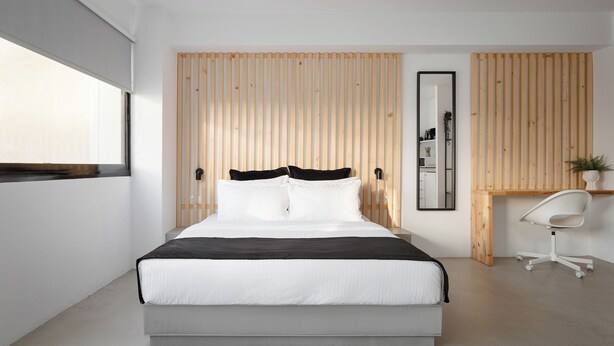 Ein modernes Schlafzimmer mit einem großen Bett, einer Wand aus Holzlatten, einem Schreibtisch mit Stuhl und einem Spiegel.