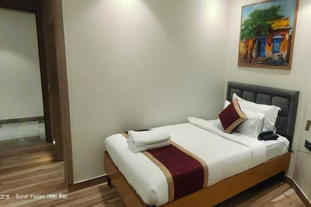 A neatly made bed with a headboard, a painting on the wall, and a door leading to another room.
