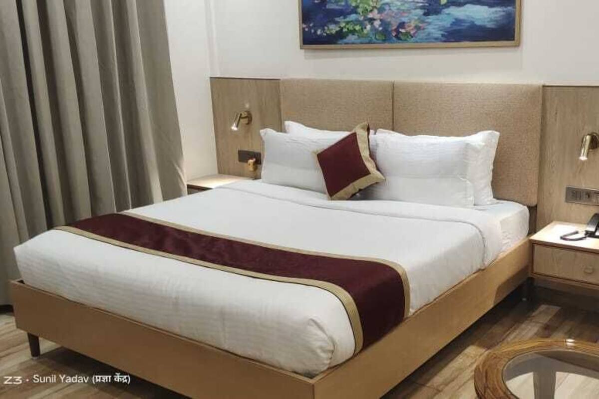 A hotel room with a large bed, a bedside table with a phone, and a small desk with two bottles of water.