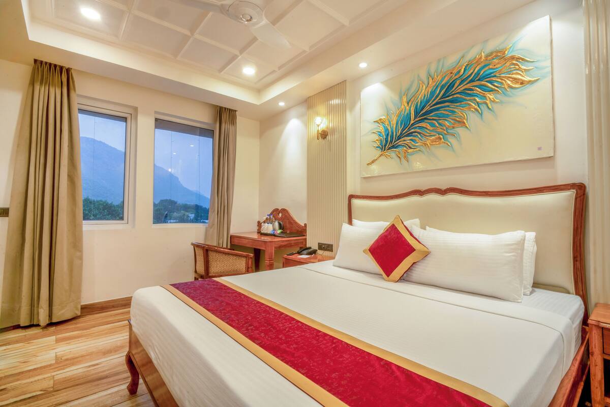 A hotel room with a large bed, a desk, a chair, and a painting on the wall.