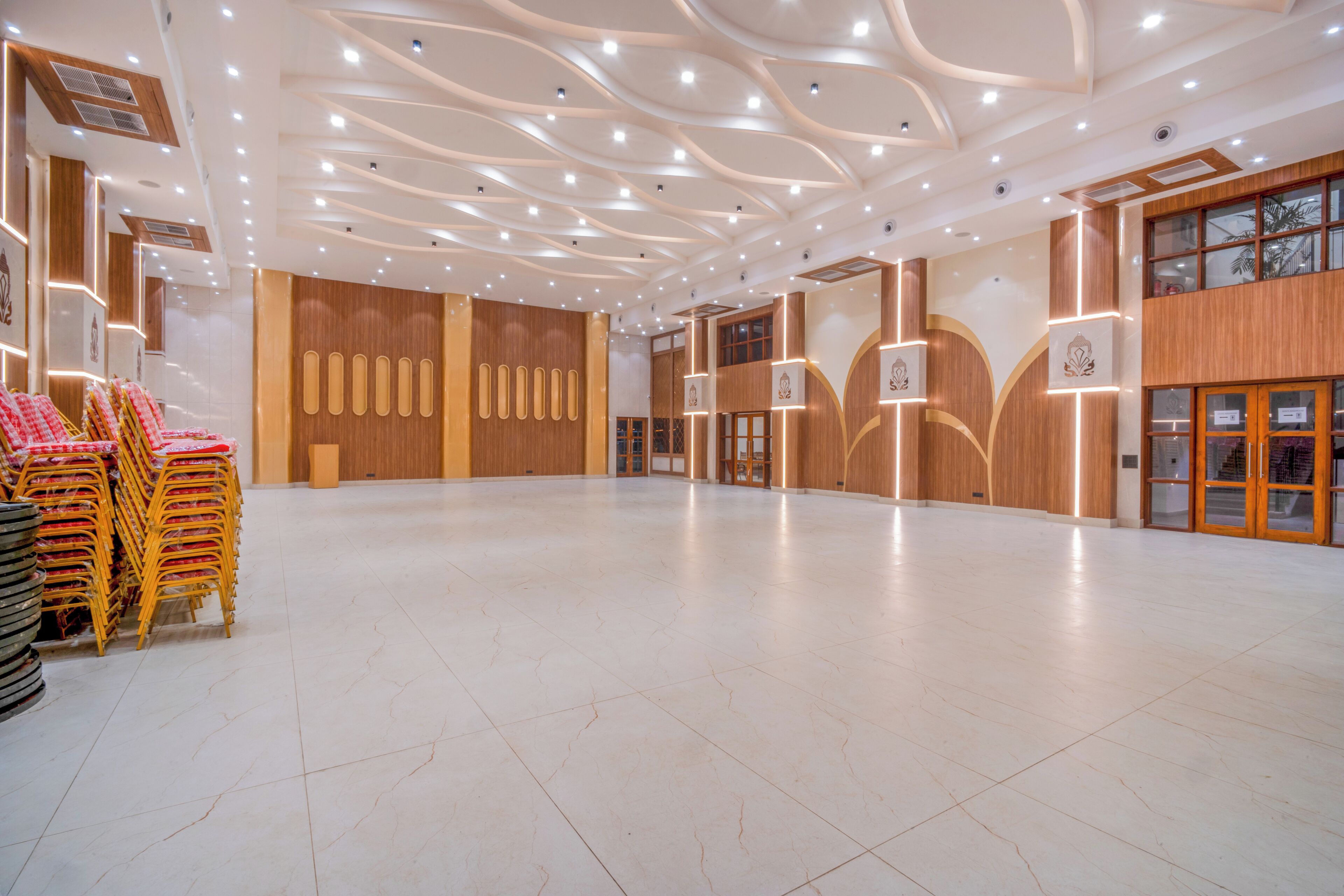 Un amplio vestíbulo de hotel con techo alto, iluminación moderna y un gran espacio abierto con una pila de sillas y mesas.